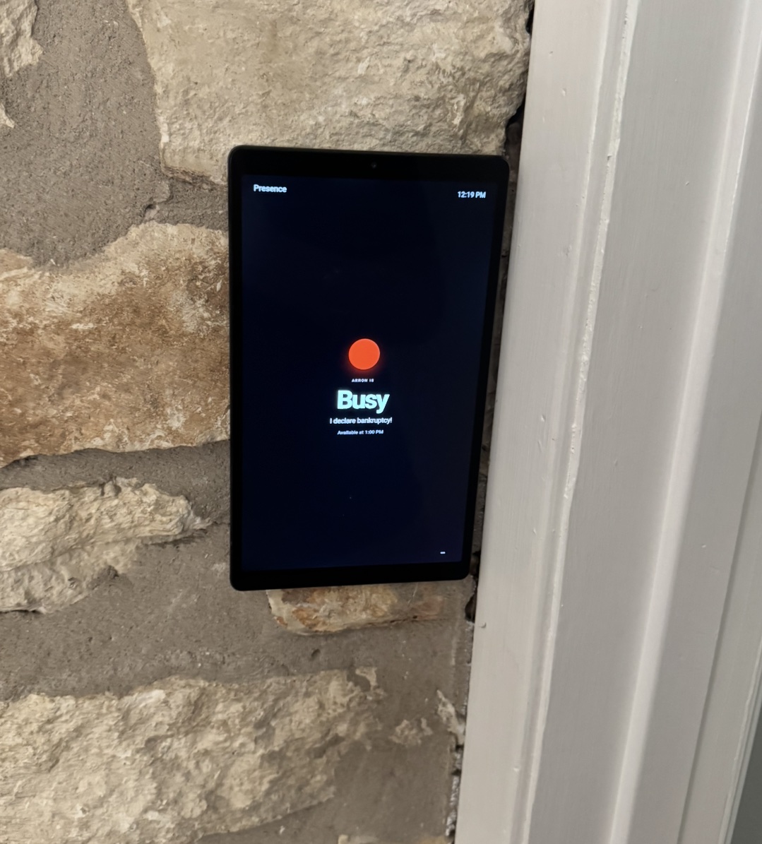 A tablet mounted beside a home office door showing a red Presence status